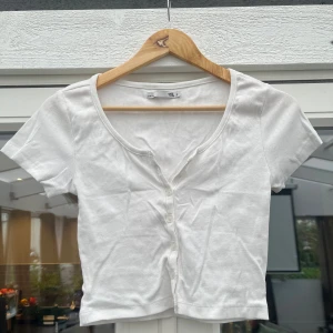 Vit ribbad kortärmad topp med knappar - Säljer en vit ribbad topp från 151 med korta ärmar och knappar framtill. Modellen är croppad och har en rund halsringning. Perfekt för dig som gillar en enkel och stilren look.