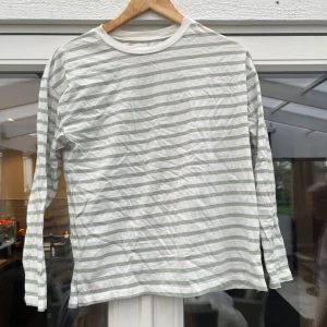 Randig långärmad tröja i bomull - Vit och ljusgrå randig långärmad tröja med rund halsringning. Tillverkad i mjuk bomull, perfekt för en avslappnad och stilren look. Passar bra till jeans eller shorts för en enkel vardagsstil.