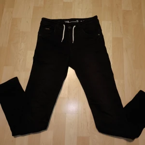 Svarta jeansbyxor med snörning - Svarta jeansbyxor från LAB Industries med vit snörning i midjan. Klassisk femficksmodell och raka ben. Byxorna har en enkel design och är tillverkade i ett stretchigt jeansmaterial för extra komfort. De är i barnstorlek 170 relaxed fit. Jeansen är i princip aldrig använda!!!