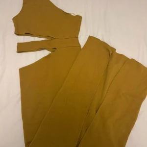 Beige gul oneshoulder långklänning - Säljer en beige långklänning med oneshoulder-design och snygga cutouts vid midjan. Klänningen är figurnära och har en stilren, modern look som verkligen sticker ut. Materialet är mjukt och stretchigt, perfekt för dig som gillar att klä dig trendigt och bekvämt.