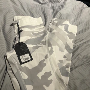 Vita camo leggings från Better Bodies storlek s  - Helt nya Snygga vita och grå camo leggings från Better Bodies med hög midja och tight passform. Tillverkade i stretchigt syntetmaterial, perfekta för gymmet eller träning. Stora loggan längs benet ger en sportig vibe.