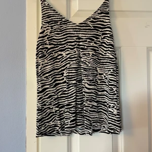 Zebramönstrad linnetopp från H&M XS - Snygg zebramönstrad linnetopp från H&M i svart och vitt. Toppen har smala axelband och v-ringning både fram och bak. Perfekt för dig som gillar djurmönster och vill sticka ut lite extra. Lätt och luftig modell som passar till många olika outfits.