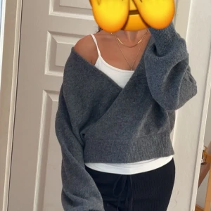 Grå omlott kofta med offshoulder - Mysig grå omlott kofta med offshoulder-look och bred ribbad kant. Koftan har en loose passform och långa ärmar, perfekt att slänga på sig över ett linne. Stickad i mjukt material och ger en chill vibe. Storlek M men passar mig som vanligtvis har S/XS. Köpte den i somras och har aldrig använt den