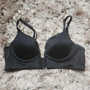 Svart bandeau tubtopp med bygel 80B - Snygg svart bandeau tubtopp med bygel och vadderade kupor. Mjuk och slät yta i stretchigt material, perfekt under tighta plagg. Stängs med hyskor bak.