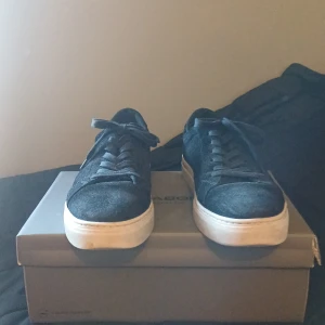 Svarta mockasneakers från Vagabond - Snygga svarta sneakers från Vagabond i mocka med klassisk rund tå och vita platta sulor. Skorna har snörning och en stilren design som passar till det mesta. Perfekta för dig som gillar en clean och enkel look med lite extra edge. Pris ej hugget i sten!