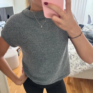 Grå stickad kortärmad tröja - Mysig grå stickad tröja med korta ärmar och högre hals. Tröjan har en enkel, rak passform och är superenkel att matcha med jeans eller kjol.