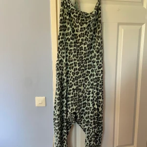 Leopardmönstrad jumpsuit från Love Forever - Cool jumpsuit med leopardmönster i svart och grått på ljus bakgrund från Love Forever. Modellen har lös passform, djup gren och breda axelband. Mjuk och stretchig bomull, perfekt för en avslappnad och trendig look. Fickor på sidorna för extra chill vibe.