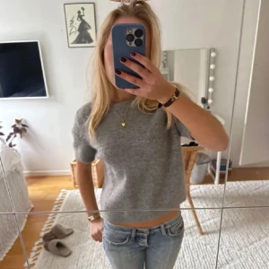 Grå stickad kortärmad tröja från Zara - Supermjuk grå stickad tröja från Zara med korta ärmar och rund hals. Tröjan har en enkel och clean look med ribbade kanter vid ärmslut och hals. Perfekt att styla med jeans eller kjol för en chill vibe.