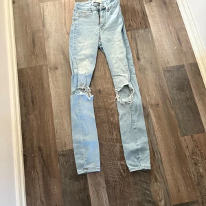 Ljusblå skinny jeans med hål - Säljer ett par ljusblå skinny jeans med slitna detaljer och stora hål på båda knäna. Jeansen har klassisk femficksdesign och dragkedjegylf. Perfekta för en avslappnad och trendig look.