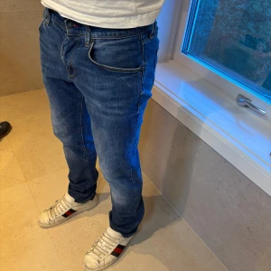 Blå jeans från Tommy Hilfiger - Säljer ett par klassiska blå jeans från Tommy Hilfiger med fem fickor och normal passform. Jeansen har en snygg tvätt med lätt slitning och raka ben. Perfekta för dig som gillar en tidlös och avslappnad stil.