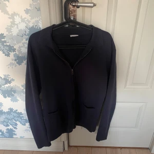 Mörkblå kofta från John Henric - Stilren mörkblå kofta från John Henric med dragkedja framtill och två fickor. Klassisk krage och långärmad modell, perfekt för lager-på-lager. Snygg och enkel att matcha till olika outfits.