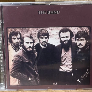 The Band (Remastered CD) - 24-bit digitalt remastrad CD av The Band, utgiven av Capitol Records. Innehåller klassiska låtar som 'The Night They Drove Old Dixie Down' och bonusspår. Fodral och skiva i mycket gott skick, inga synliga repor eller skador.
