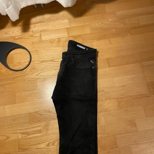 Svarta Replay jeans Rocco, stl 31 - Svarta jeans från Replay, modell Rocco, med klassisk femficksdesign och diskreta Replay-detaljer på fickorna. Jeansen har en smal passform och är tillverkade i stretchigt bomullsmaterial för extra komfort. Perfekta för dig som gillar en stilren look.