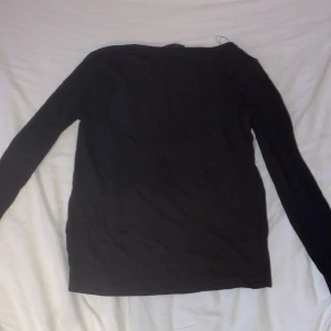 Svart långärmad tröja från 157 - En basic svart långärmad tröja från 157. Tröjan har en enkel och rak passform med rund halsringning och är tillverkad i mjuk bomull. Perfekt att styla med jeans eller under en hoodie för lager-på-lager-look.