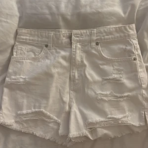 Vita jeansshorts - Snygga vita jeansshorts från For Sister med hög midja, slitna detaljer och fransig kant nedtill. Klassisk femficksmodell med råa kanter och coola slitningar framtill och baktill. Perfekta för en avslappnad och trendig look i sommar.