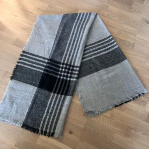 Rutig halsduk från Gina Tricot - Stor och mjuk halsduk från Gina Tricot i grått och svart med klassiskt rutigt mönster. Materialet är stickat och har fransar längs kanterna. Perfekt att svepa runt halsen för en chill och stilren look.