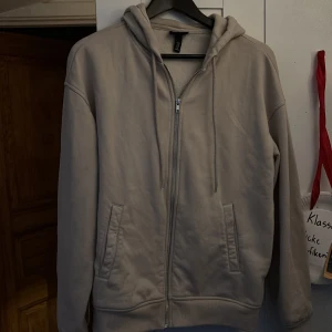 Beige hoodie med dragkedja från H&M - Säljer en beige hoodie från H&M i loose fit med dragkedja framtill och två fickor. Hör av er vid intresse!
