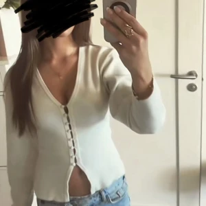 Vit kofta med knappar från Gina Tricot - Säljer en stilren vit kofta från Gina Tricot i storlek XS. Koftan har v-ringning, klädda knappar framtill och är tillverkad i ett mjukt, stickat material. lite uttöjd i knappen högst upp men inget man märker av riktigt!