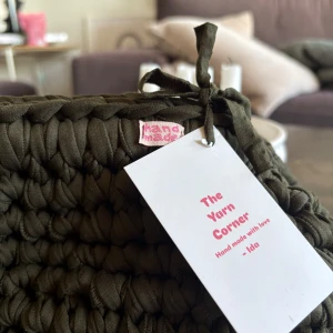 Handgjord grön stickad kuvertväska - Unik handgjord kuvertväska i mörkgrönt, grovstickat tyg. Väskan har en rektangulär form och är tillverkad av mjukt bomullsmaterial. Perfekt för dig som gillar personliga accessoarer med en cool, chunky look. Märkt med 'hand made' och knytband upptill.