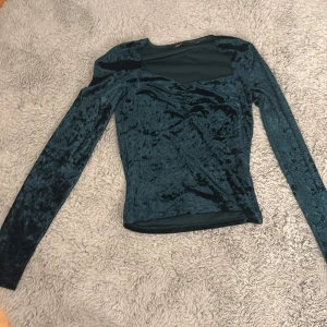 Mörkgrön sammetstopp med meshdetalj - Snygg mörkgrön topp i sammet med lång ärm och meshparti upptill. Figurnära passform och rund halsringning. 