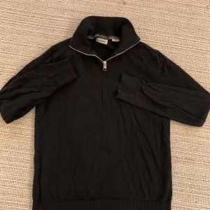 Svart half zip tröja från Jack & Jones - Svart långärmad tröja från Jack & Jones med hög krage och half zip-dragkedja. Tröjan har ribbade muddar vid ärmslut och nederkant, vilket ger en snygg och stilren look. Perfekt för lager-på-lager under höst och vinter.