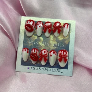 VampKiss (XS);Short Almond;Curved - Snygga handgjorda press-on naglar i mandelform med skimrande vit bas och 3D-detaljer i rött, som läppar, rosetter och droppar. Perfekt för dig som vill sticka ut med en unik och kreativ look. Kommer i storlek XS: 14 mm, 11 mm, 11,5 mm, 10 mm, 8 mm 