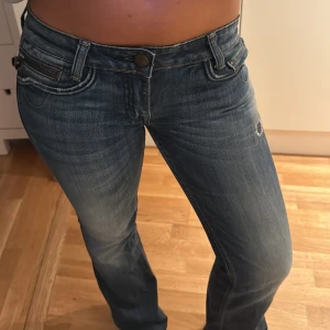 Blå bootcut jeans från Rerock Express - Snygga blå bootcut jeans från Rerock for Express med broderade bakfickor och slitningar framtill. Jeansen har låg midja och klassisk femficksdesign. Skit snygga fickor baktill, dessa jeans är as coola. Har klippt av dom lite så passar någon som är ca 165cm och neråt. Storlek w27