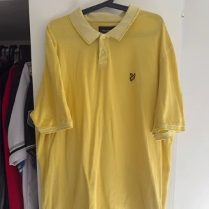 Gul pikétröja från Lyle & Scott - Snygg gul pikétröja från Lyle & Scott i storlek XXL. Klassisk krage med knappar och den ikoniska fågel-loggan broderad på bröstet. Tillverkad i mjuk bomull som känns skön mot huden. Perfekt för dig som gillar stilrena och färgglada plagg.