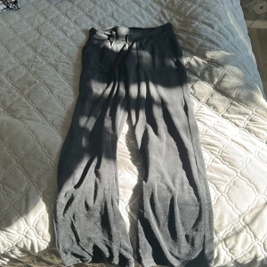 Svarta mjukisbyxor från 157, storlek S - Svarta mjukisbyxor från 157 med breda ben och dragsko i midjan. Byxorna har fickor både fram och bak och är gjorda i ett mjukt, syntetiskt material som känns skönt mot huden. Perfekta för en chill och avslappnad stil.