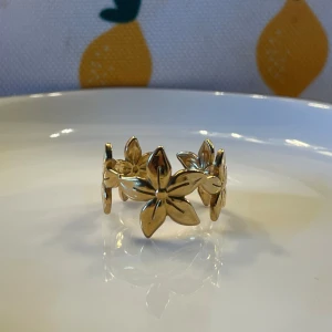 Guldig ring med blommor - Superfin ring i guldton med flera sammankopplade blommor runt hela bandet. Blommorna har fem blad och ger en cool och lekfull vibe. Perfekt accessoar för dig som vill sticka ut lite extra.