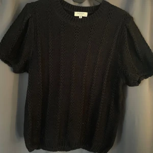 Svart stickad tröja  - Säljer en svart stickad tröja med korta puffärmar och rund halsringning. Tröjan har ett snyggt hålmönster i lodräta rader och ribbade kanter. Jätte fin och perfekt till hösten. Säljs för att den inte kommer till användning. Kontakta för egna bilder.