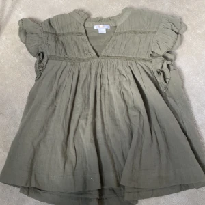 Olivgrön blus från Gina Tricot - Säljer en olivgrön blus från Gina Tricot i storlek 158/164. Blusen har volangdetaljer vid ärmarna, v-ringning och är tillverkad i ett lätt och luftigt tyg. Har inte använt innan 