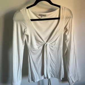Vit omlottopp med knyt från design by si  - Säljer en vit långärmad omlottopp från Pieces med snygg knytning framtill. Toppen har djup v-ringning och är tillverkad i mjukt, stretchigt material som sitter skönt på kroppen. Perfekt för dig som gillar stilrena och trendiga plagg.