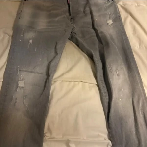 Grå Dsquared2 jeans med slitningar - Snygga grå jeans från Dsquared2 med slitna detaljer och diskreta färgstänk. Klassisk femficksmodell med smal passform och låg midja. Perfekta för dig som gillar en edgy streetstil och vill sticka ut lite extra.