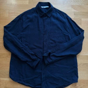 Mörkblå skjorta från Zara i bomull - Snygg mörkblå skjorta från Zara i bomull med klassisk krage, bröstficka och knäppning framtill. Skjortan har långa ärmar med knappar vid manschetten och en avslappnad passform. Perfekt för en stilren och enkel look.