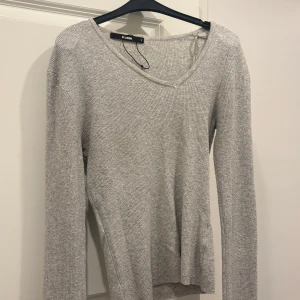 Ljusgrå ribbad tröja från BikBok - Supermjuk och stilren ljusgrå ribbad tröja från BikBok. Tröjan har v-ringning, lång ärm och en figurnära passform. Perfekt att matcha med jeans eller kjol för en clean look.
