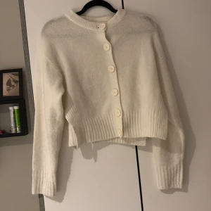 Vit croppad kofta från 157 - Supermysig vit kofta från 157 i croppad modell med stora knappar framtill. Tröjan har långärmade ribbade muddar och är stickad för extra mjuk känsla. Perfekt att slänga på sig när det är lite kyligt ute.