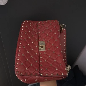 Röd Valentino rockstud väska  - Säljer denna valentino  väska inköpt för ca 20.000kr. Perfekt för dig som vill sticka ut med en trendig accessoar. Materialet är skinn och väskan har en lyxig känsla. Medkommer gör äkthetsbevis, dustbag och box. 