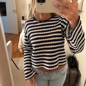 Randig stickad tröja i blått och vitt - Säljer en mysig stickad tröja med breda marinblå och vita ränder. Tröjan har långärmade ärmar och en croppad passform som ger en chill vibe. Materialet är grovstickat och känns mjukt mot huden. Perfekt för dig som gillar en avslappnad och trendig stil.