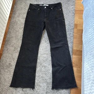 Svarta bootcut jeans från MNG - Svarta jeans från MNG i modellen Fiona, med bootcut-ben, fransiga benslut. Klassisk femficksdesign och knappgylf. Jeansen har en snygg mörk tvätt och är tillverkade i ett stadigt denimtyg.