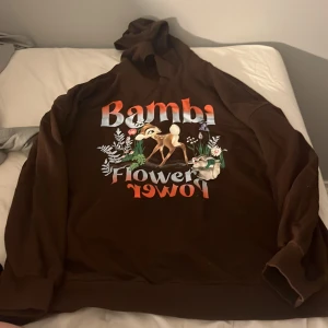 Brun Bambi hoodie med tryck - Säljer en brun hoodie med stort Bambi-tryck och texten 'Bambi Flower Power' på framsidan. Tröjan har huva och långa ärmar. Perfekt för dig som älskar Disney. Vet ej vart den är köpt då lappen är bortklippt. Inga fläckar och ska självklart tvättas innan den säljs! Hör av er vid frågor/intresse💕