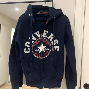 Mörkblå Converse hoodie S/xl - Säljer en mörkblå hoodie från Converse i storlek XL i barn storlek men runt en S i vuxen. Tröjan har dragkedja, huva med snörning och stor logga framtill. Fodrad insida för extra värme och klassiska kängurufickor. Perfekt för dig som gillar streetwear och sportig stil.