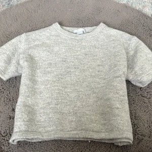 Grå stickad tröja från Gina Tricot - Mysig grå stickad tröja från Gina Tricot i storlek 146/152. Tröjan har korta ärmar, rund halsringning och en enkel, stilren design som passar perfekt till lager-på-lager. Perfekt för kyliga dagar när du vill vara både bekväm och snygg. Lite liten i storlek