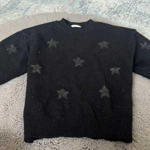 Svart stickad tröja med stjärnor Gina Tricot storlek 146/152 - Svart stickad tröja från Gina Tricot med snygga svarta stjärnor över hela framsidan. Tröjan har ribbade muddar vid hals, ärmslut och nederkant. Perfekt för dig som gillar en enkel men cool look.