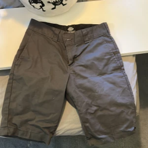 Grå shorts från Dickies '67 Collection - Säljer ett par grå shorts från Dickies '67 Collection. Klassisk rak modell med midwaist och praktiska fickor fram. Materialet är slitstark bomull, perfekt för dig som gillar streetwear och enkel stil. Stängs med knapp och dragkedja.