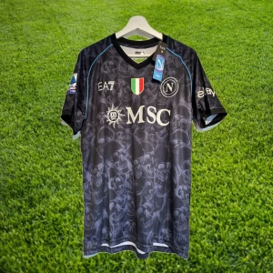 Napoli EA7 Special Edition Halloween fotbollströja - Säljer en svart/blå Napoli fotbollströja från EA7 Special Edition med Serie A-märke på ärmen och klubbmärke på bröstet. Tröjan har korta ärmar, diskret dödskallemönster och blå detaljer längs axlarna. Perfekt efter deras ligatitel!
