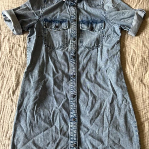 Jeansklänning med korta ärmar - Snygg jeansklänning med korta ärmar och knappar framtill. Två bröstfickor med knappstängning ger en cool look. 