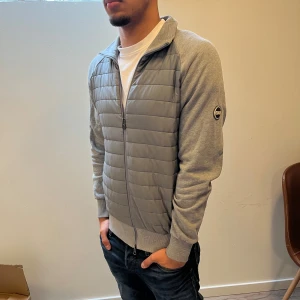 Grå cardigan jacka från Colmar - Snygg grå jacka från Colmar med quiltad front och rygg, samt mjuka ärmar och sidor i sweatshirtmaterial. Jackan har hel dragkedja och ribbade muddar. Perfekt för dig som gillar en clean och sportig look. NYPRIS:3999Kr, Mitt pris:1399Kr ✅