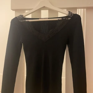 Svart ribbad topp med spets från Anna Field - Svart långärmad topp från Anna Field med ribbad struktur och v-ringning dekorerad med snygg spetsdetalj. Toppen har en figurnära passform och är perfekt för dig som gillar stilrena och feminina plagg. Materialet är mjukt och stretchigt för extra komfort.