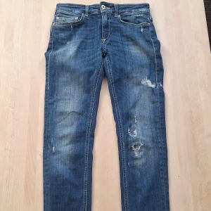 Blå Dondup Monroe jeans med slitningar - Säljer ett par blå Dondup Monroe jeans med snygga slitningar och kontrastsömmar. Klassisk femficksmodell med läderpatch bak i midjan och coola detaljer på bakfickorna. 